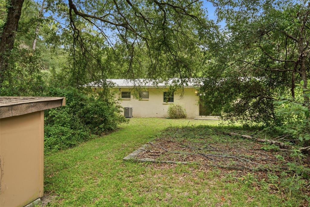 A view of the back of a single-story house surrounded by trees and overgrown vegetation — 9955 S FORESTLINE AVENUE, INVERNESS, FL