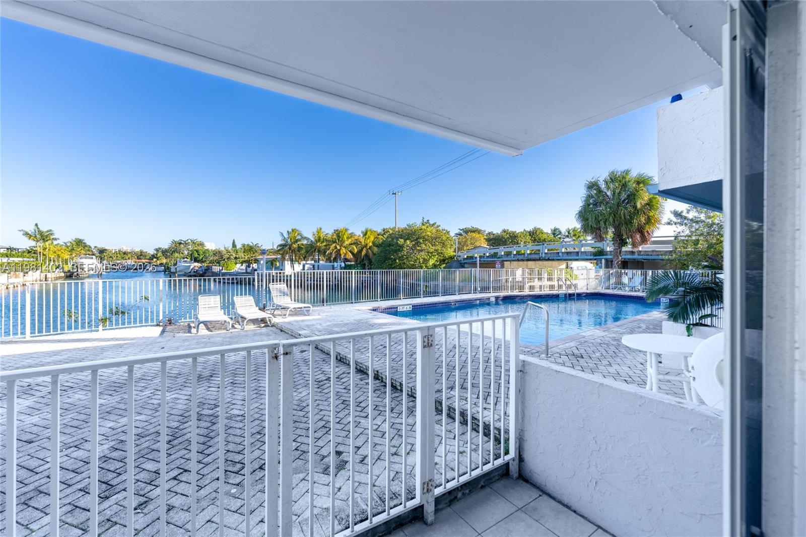 A patio overlooks a swimming pool, a white metal fence, and a canal with boats — 2225 NE 123rd St # 114, North Miami FL 33181, NORTH MIAMI, FL