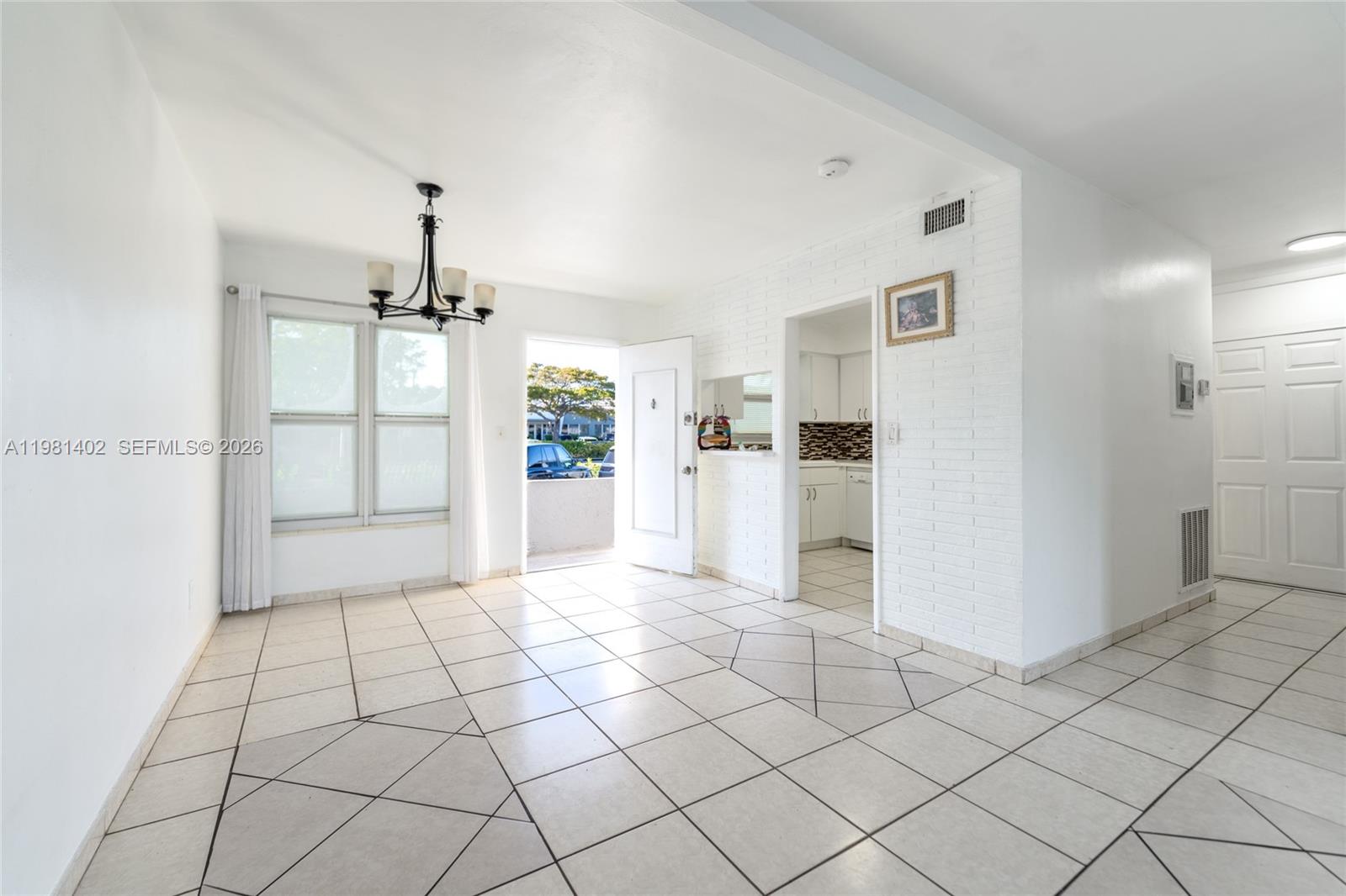 A bright living area features white tile floors, a brick accent wall, and a chandelier — 2225 NE 123rd St # 114, North Miami FL 33181, NORTH MIAMI, FL