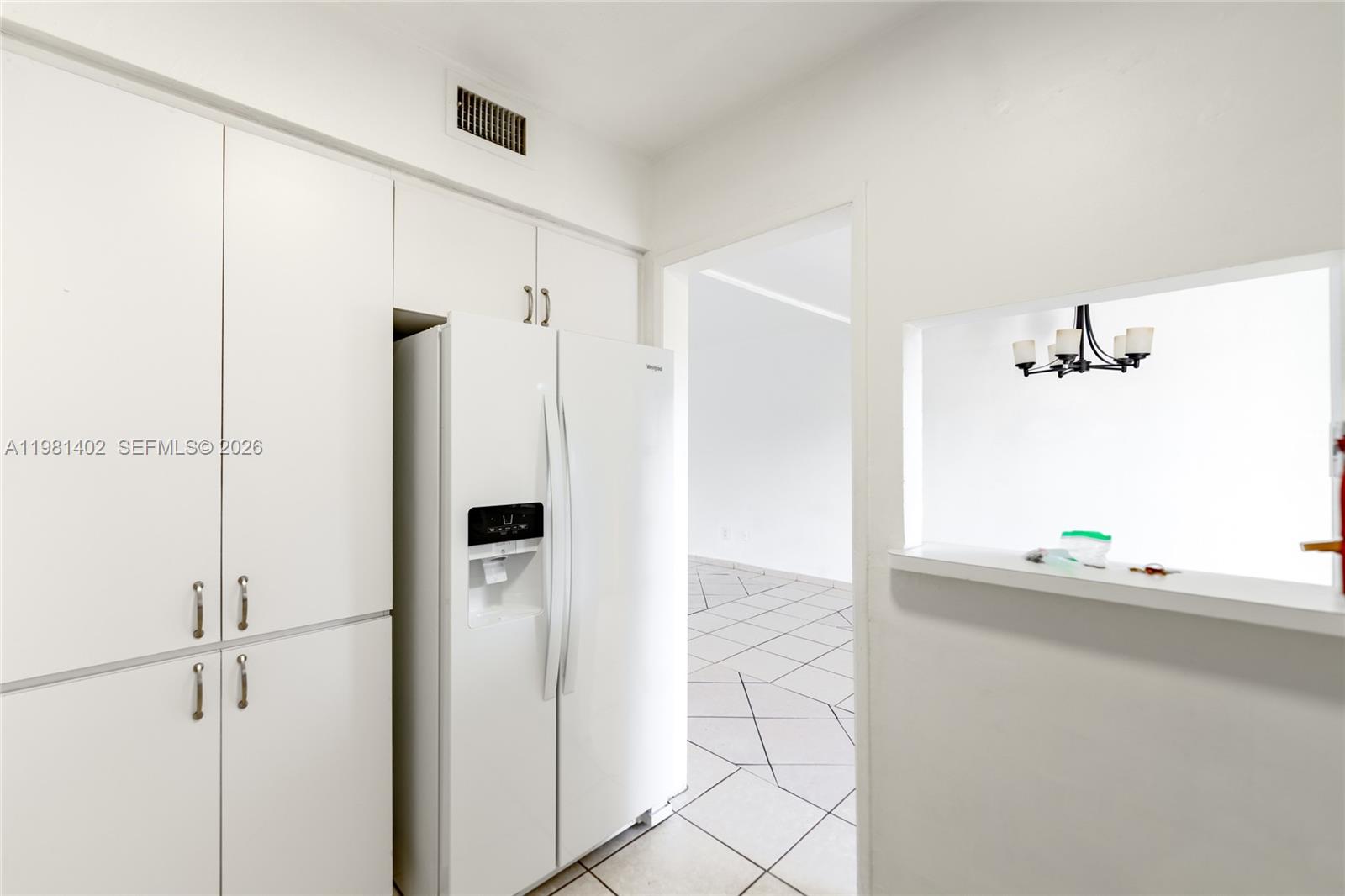 A white kitchen features a refrigerator, cabinetry, and a pass-through window to another room — 2225 NE 123rd St # 114, North Miami FL 33181, NORTH MIAMI, FL