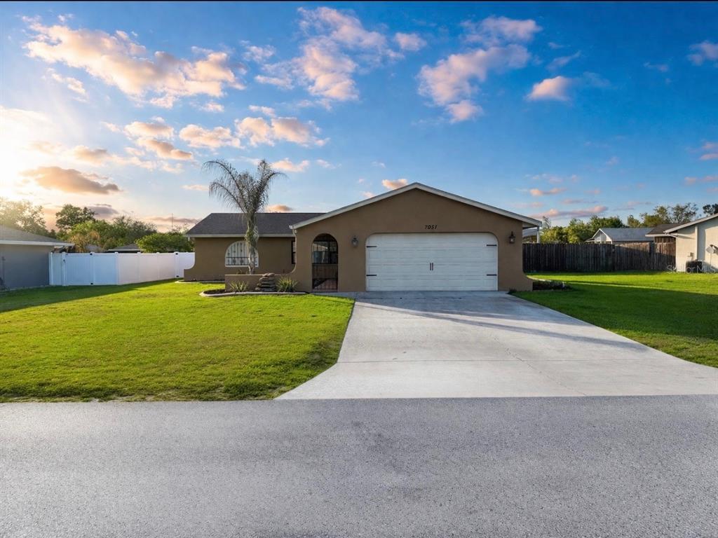 A tan single-story house with a two-car garage and a concrete driveway under a sky — 7051 LEXINGTON CIR, BROOKSVILLE, FL