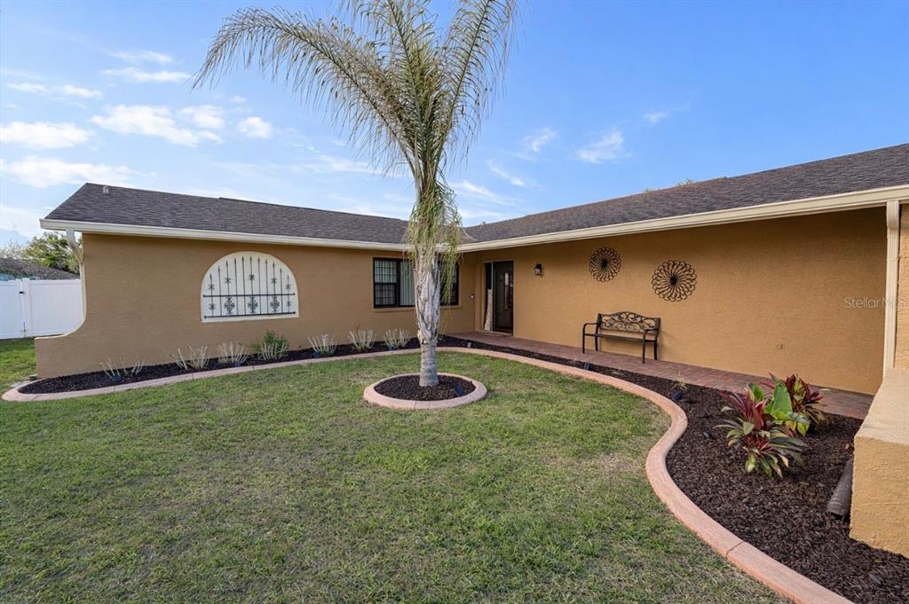 A tan house exterior features a palm tree, a curved garden bed, and a bench — 7051 LEXINGTON CIR, BROOKSVILLE, FL
