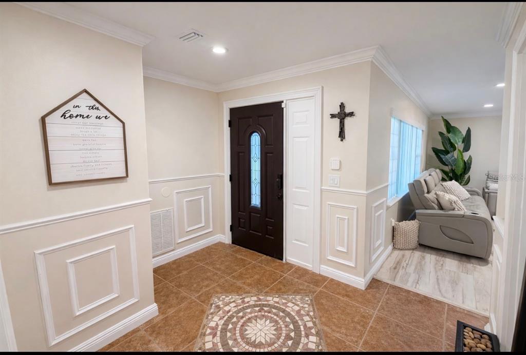 An entryway with tile flooring, wainscoting, a dark front door, and a cross wall decoration — 7051 LEXINGTON CIR, BROOKSVILLE, FL
