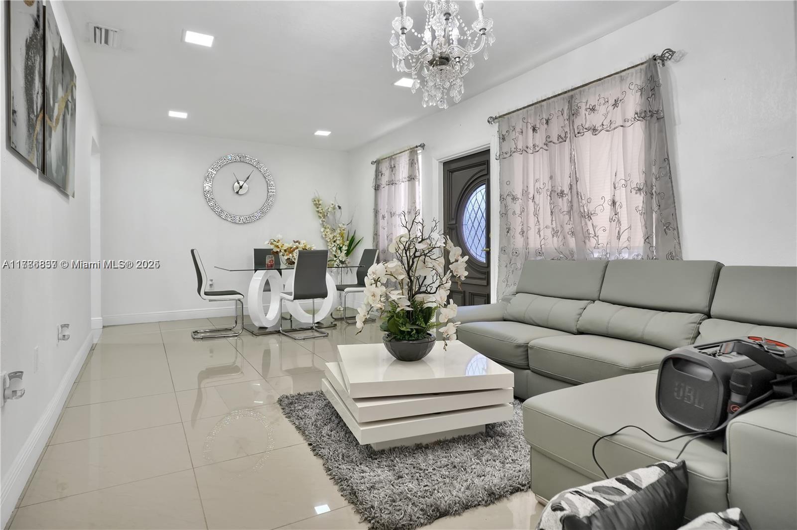 A living and dining area features tile floors, a grey sectional sofa, and a chandelier — 7225 SW 21st St, Miami FL 33155, MIAMI, FL