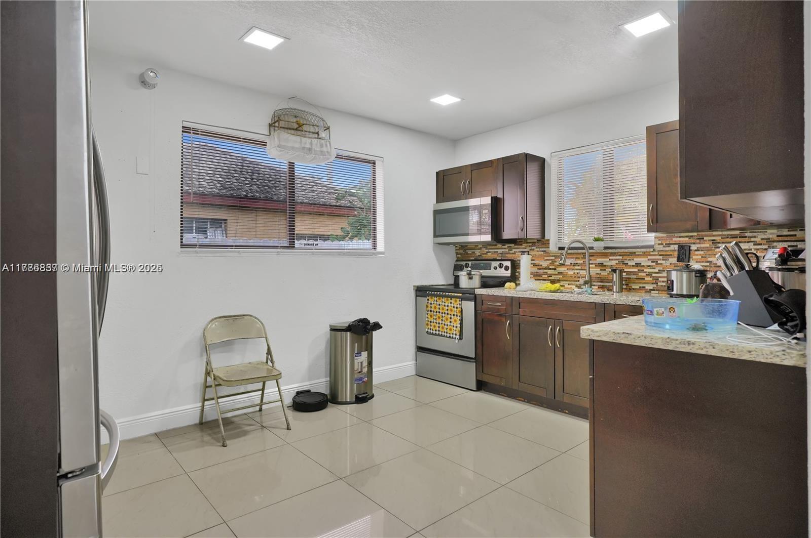 A kitchen features dark wood cabinets, granite countertops, stainless steel appliances, and light tile flooring — 7225 SW 21st St, Miami FL 33155, MIAMI, FL
