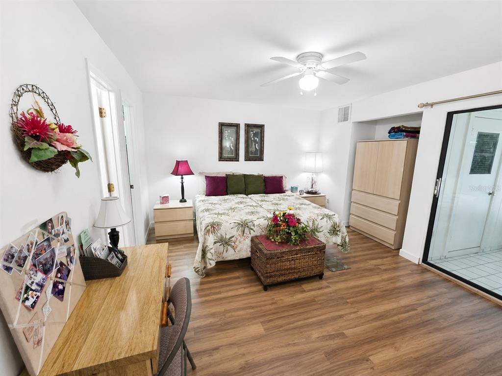 A bedroom features a bed with a tropical quilt, wood-look flooring, and a sliding glass door — 225 OAK HILL DRIVE UNIT 10, SARASOTA, FL