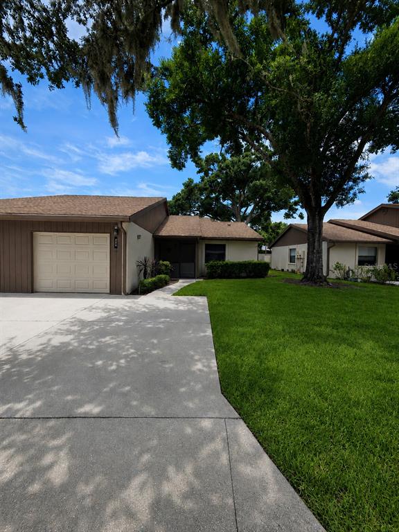 A concrete driveway leads to a one-story house with a garage and a large tree — 225 OAK HILL DRIVE UNIT 10, SARASOTA, FL