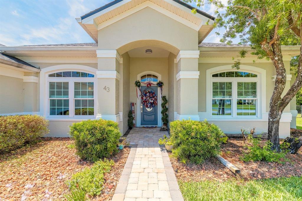 A paved walkway leads to the front entrance of a single-story house with beige siding — 43 EASTWOOD DRIVE, PALM COAST, FL