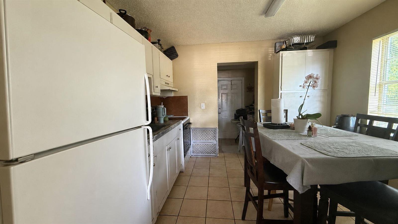 A kitchen with white appliances, light-colored cabinets, tile flooring, and a dining table — 134 Jennings Avenue # 134, FL 33463, FL