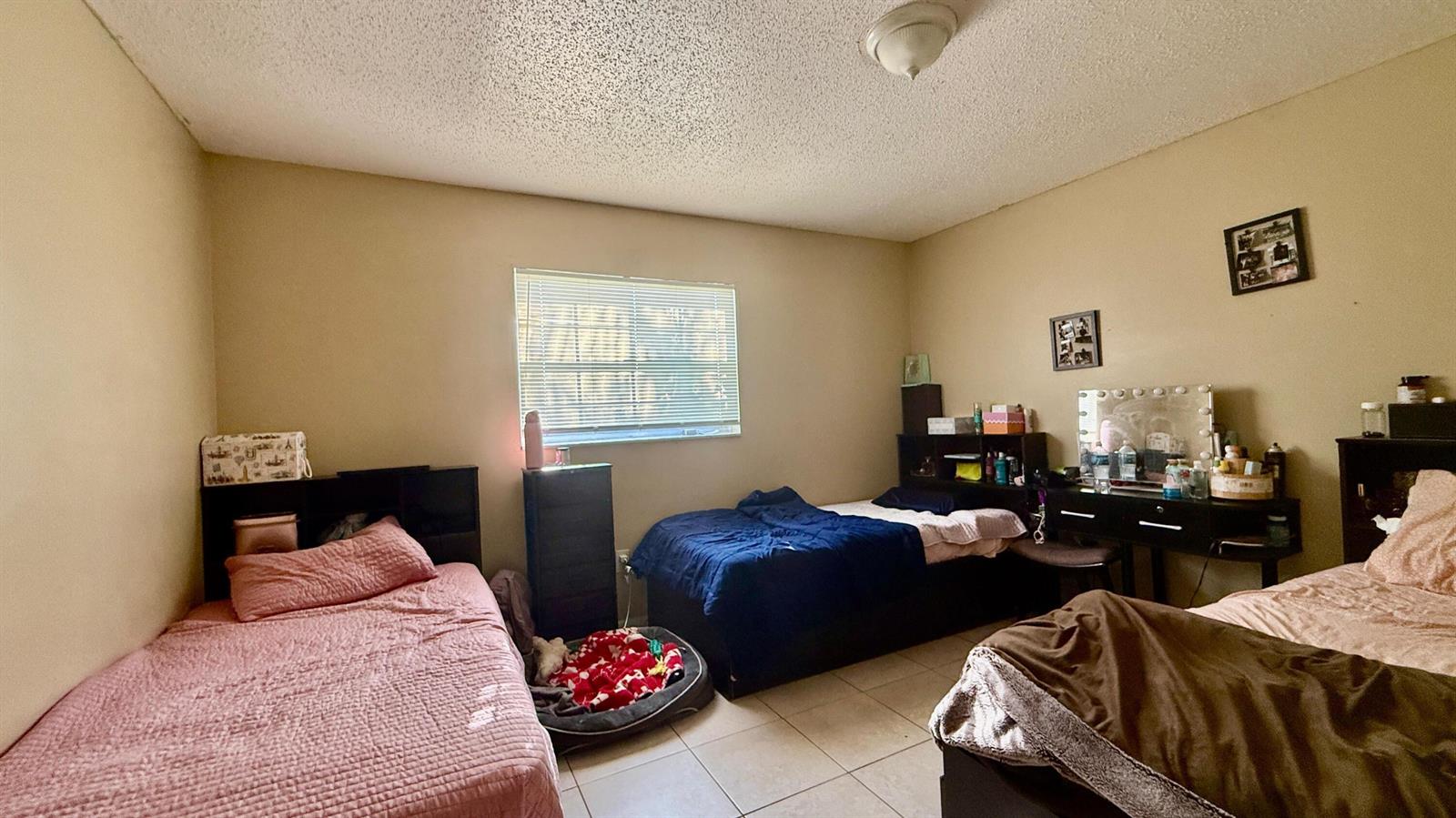 A bedroom features three beds, tile flooring, a window with blinds, and a vanity desk — 134 Jennings Avenue # 134, FL 33463, FL