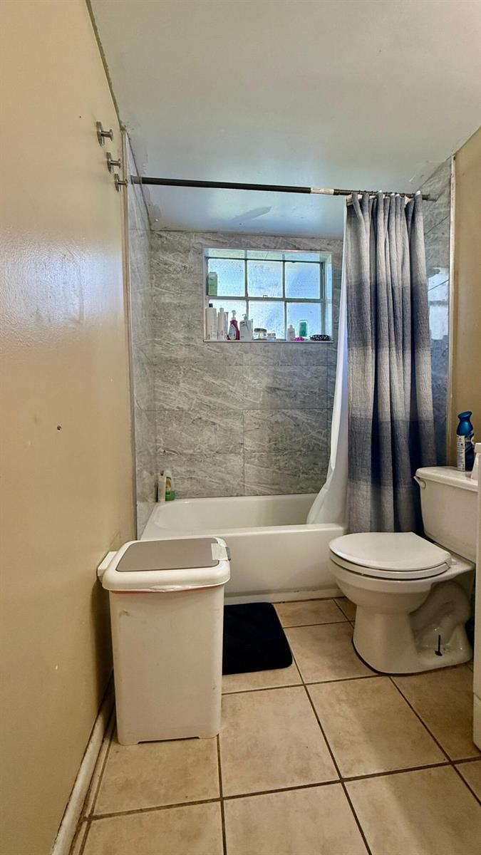 A bathroom features a tiled bathtub shower combo, a toilet, and beige floor tiles — 134 Jennings Avenue # 134, FL 33463, FL