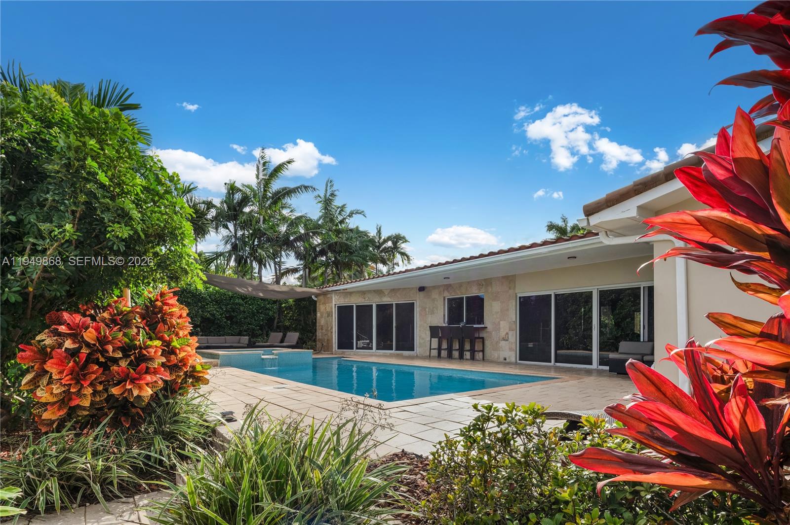 A backyard features a rectangular swimming pool with a stone patio and a covered patio area — 1155 S Biscayne Point Rd, Miami Beach FL 33141, MIAMI BEACH, FL