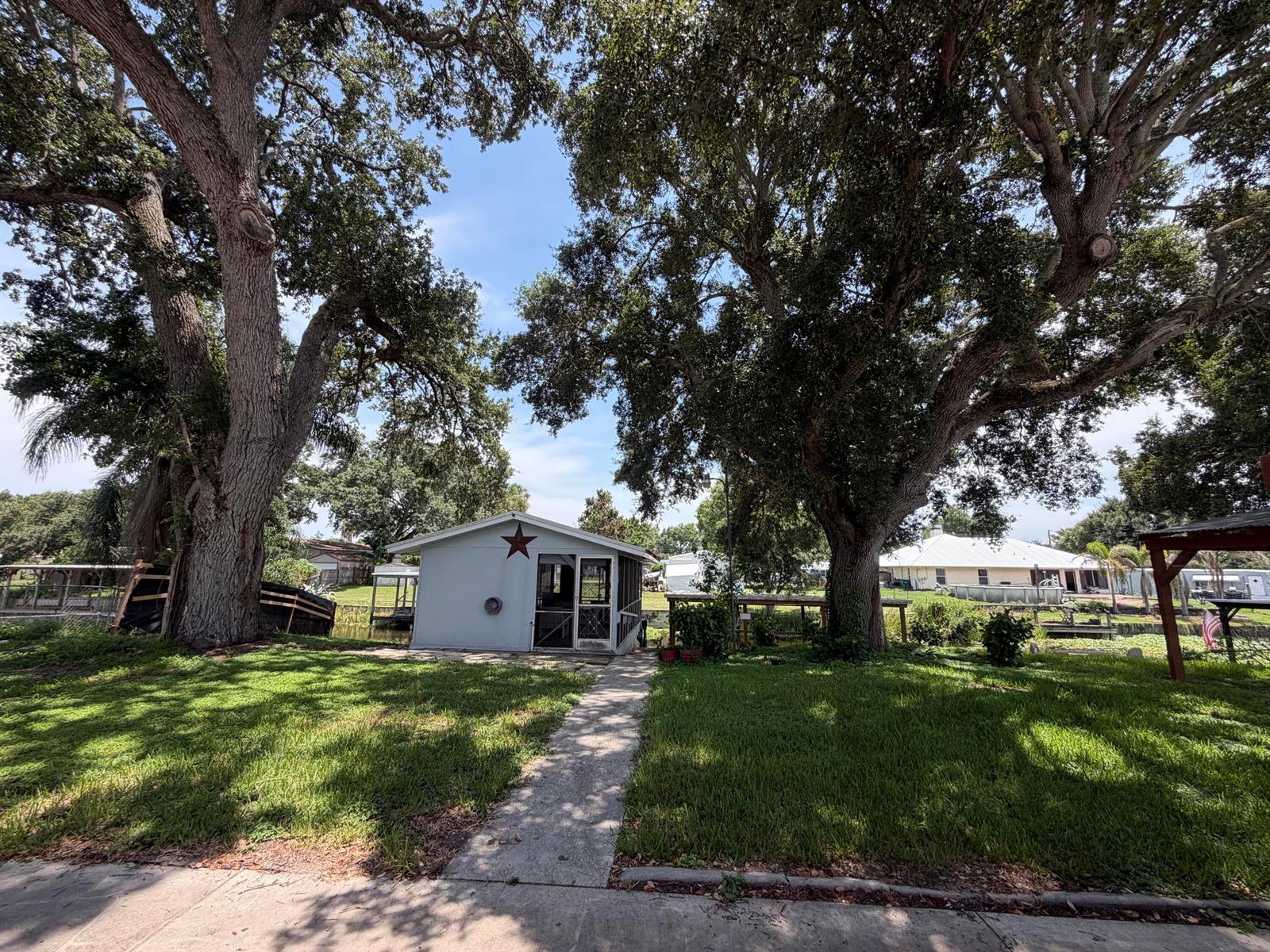 A small light-colored shed with a star decoration sits between two large oak trees — 3212 SE 24th Street, Okeechobee FL 34974, OKEECHOBEE, FL