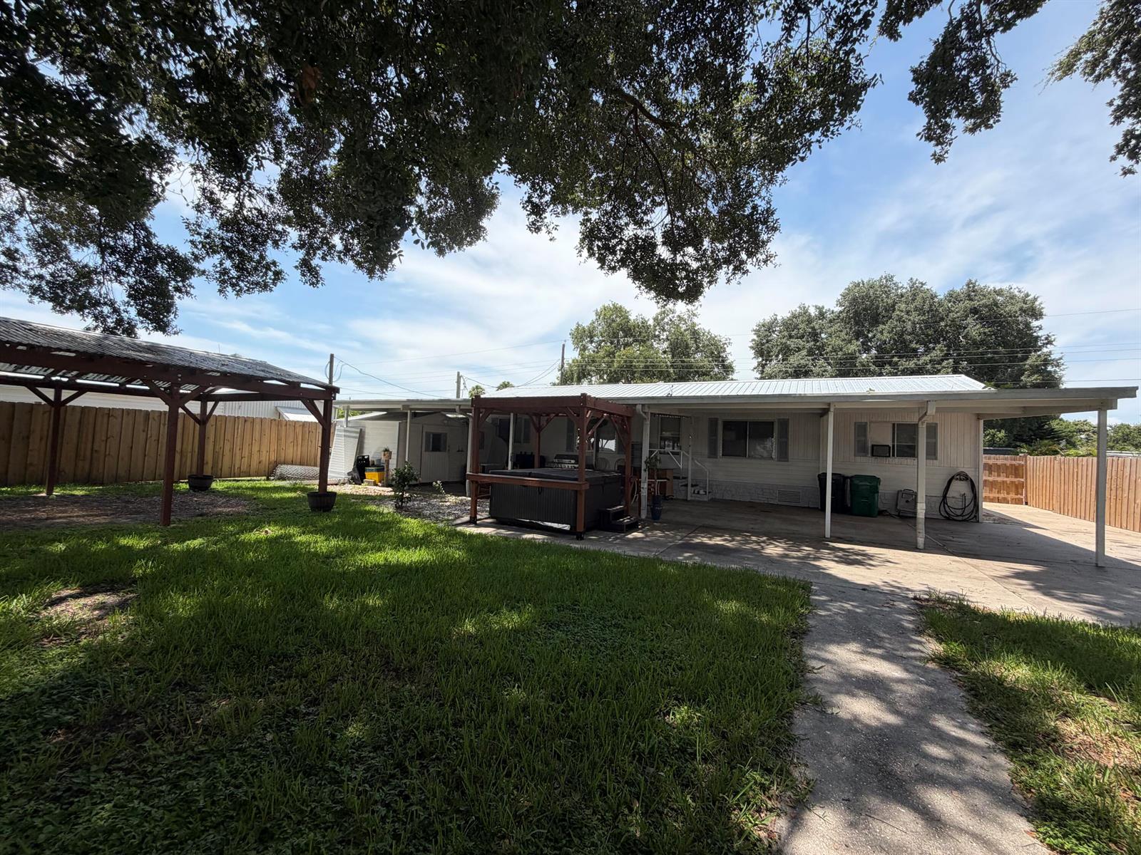A backyard features a grassy lawn, a wooden pergola, a hot tub, and a house — 3212 SE 24th Street, Okeechobee FL 34974, OKEECHOBEE, FL