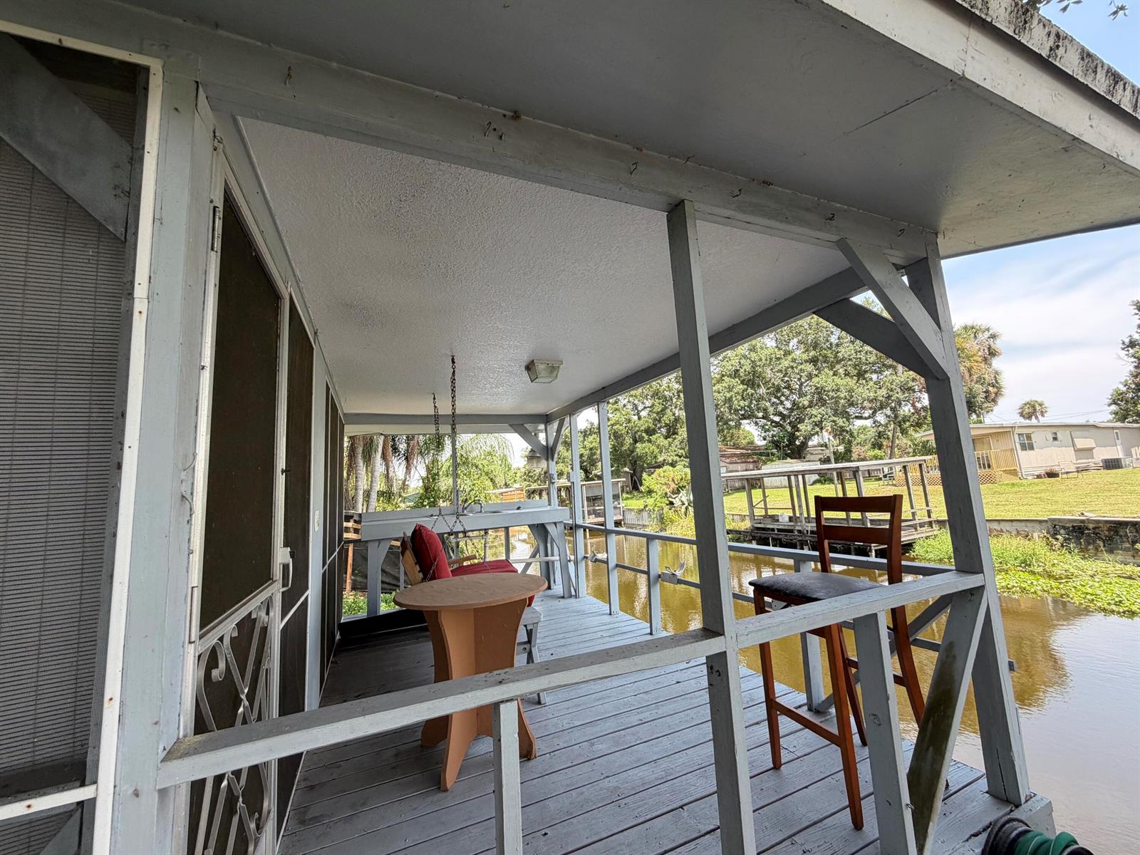 A covered wooden deck overlooks a canal with a small table and a bar stool — 3212 SE 24th Street, Okeechobee FL 34974, OKEECHOBEE, FL