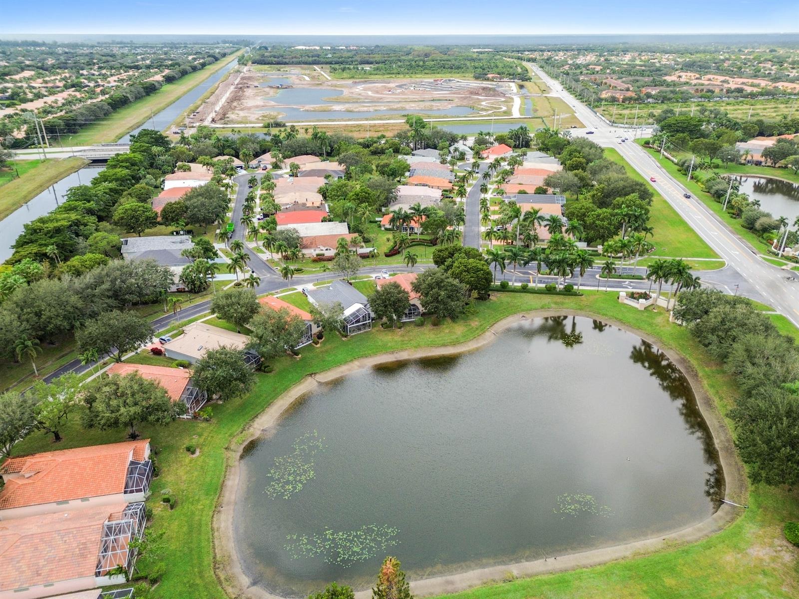 An aerial view shows a residential neighborhood with houses surrounding a large pond — 6451 Tiara Drive, Boynton Beach FL 33437, BOYNTON BEACH, FL