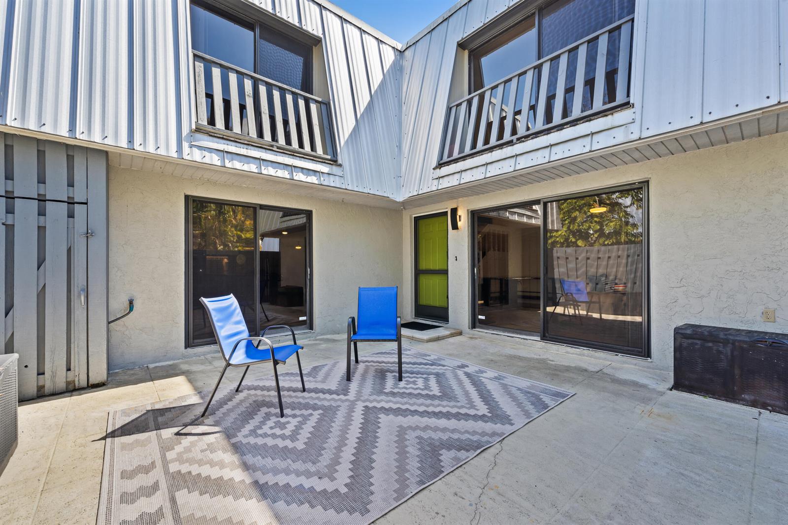 A concrete patio features two blue chairs on a patterned rug outside a two-story building — 3852 Jefferson Street, Stuart FL 34997, STUART, FL