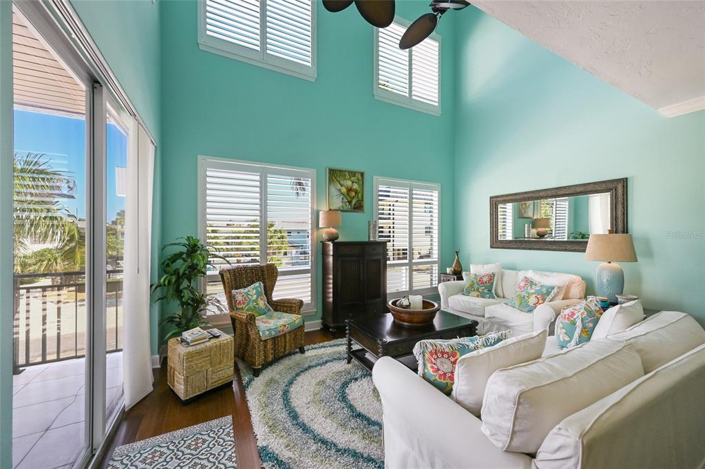 A living room with high ceilings, light blue walls, white furniture, and a balcony view — 109 6TH STREET N UNIT A, BRADENTON BEACH, FL