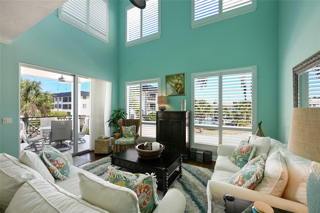 A living room with high ceilings, teal walls, white sofas, and plantation shutters on the windows — 109 6TH STREET N UNIT A, BRADENTON BEACH, FL