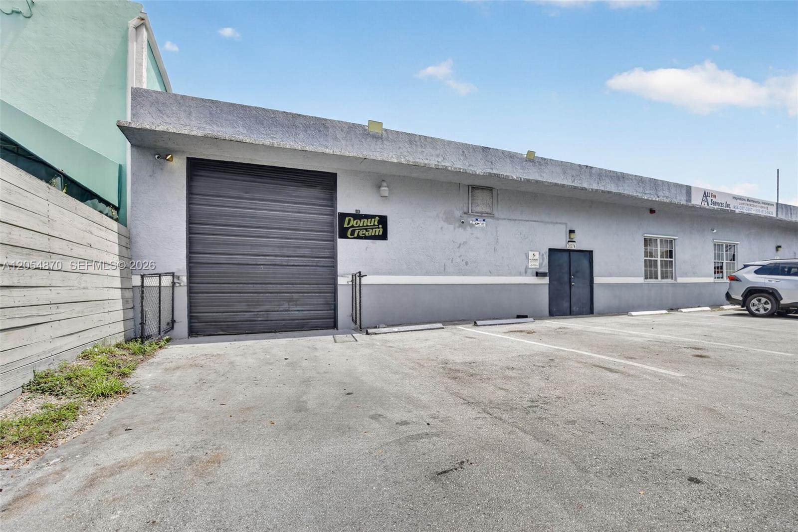 The exterior of a commercial building features a roll-up door, a pedestrian door, and parking — 2027 Sherman St # B, Hollywood FL 33020, HOLLYWOOD, FL