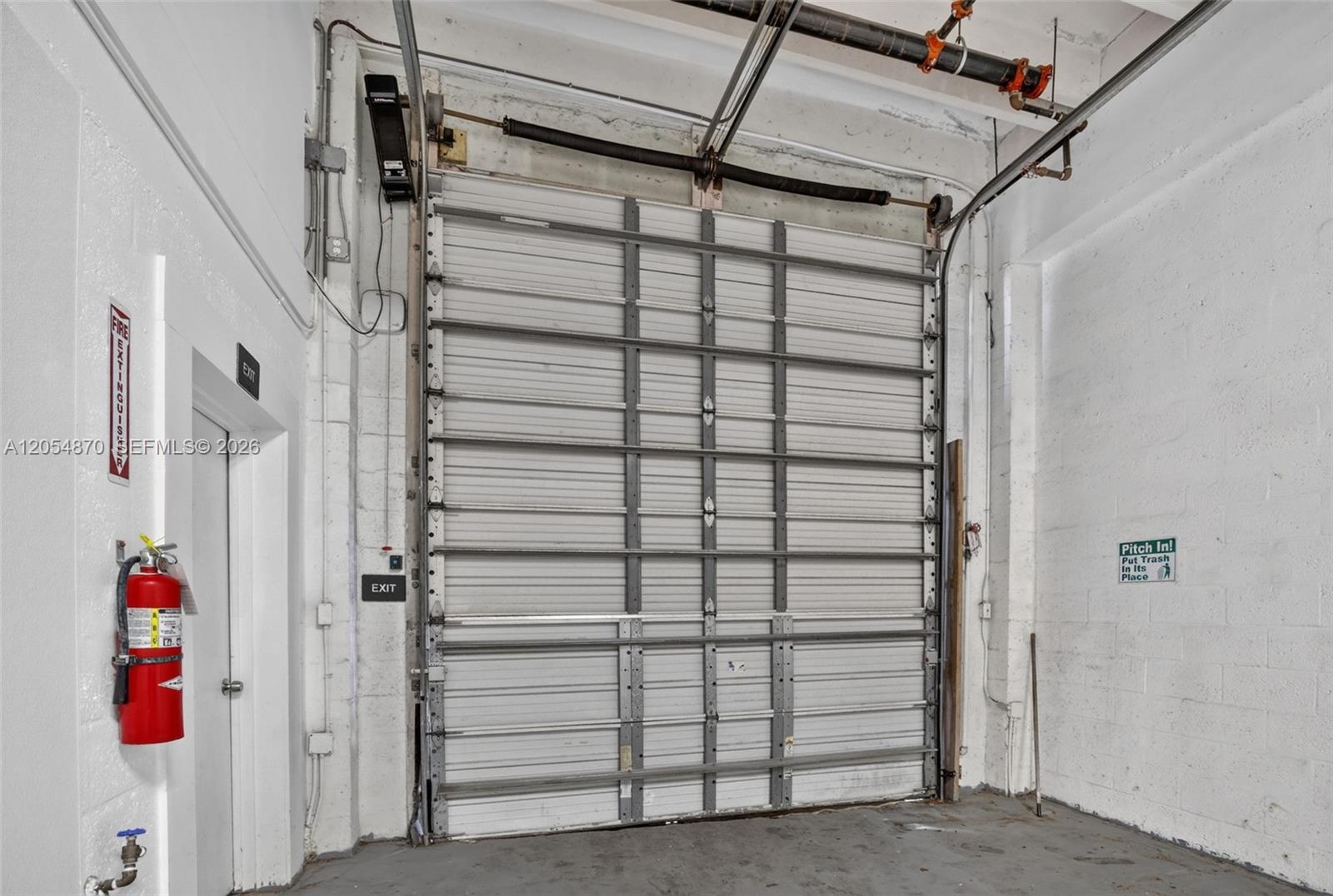 A commercial warehouse space features a large roll-up metal door, white walls, and a fire extinguisher — 2027 Sherman St # B, Hollywood FL 33020, HOLLYWOOD, FL