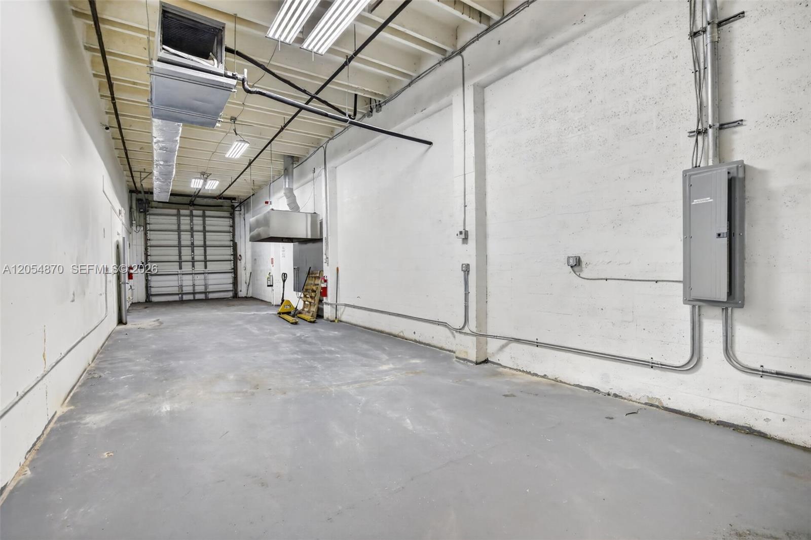 An empty industrial warehouse space features a concrete floor, white walls, and a roll-up door — 2027 Sherman St # B, Hollywood FL 33020, HOLLYWOOD, FL