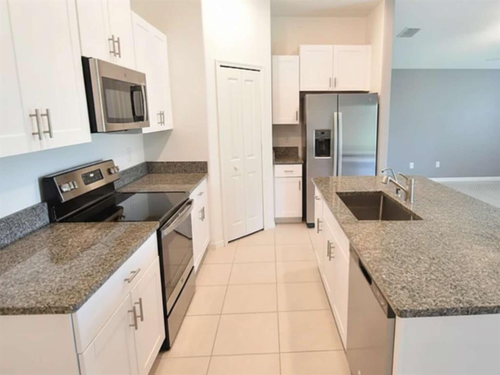 A kitchen features white cabinets, granite countertops, stainless steel appliances, and a central island — 9685 BRANCHING SHIP TRACE, WESLEY CHAPEL, FL
