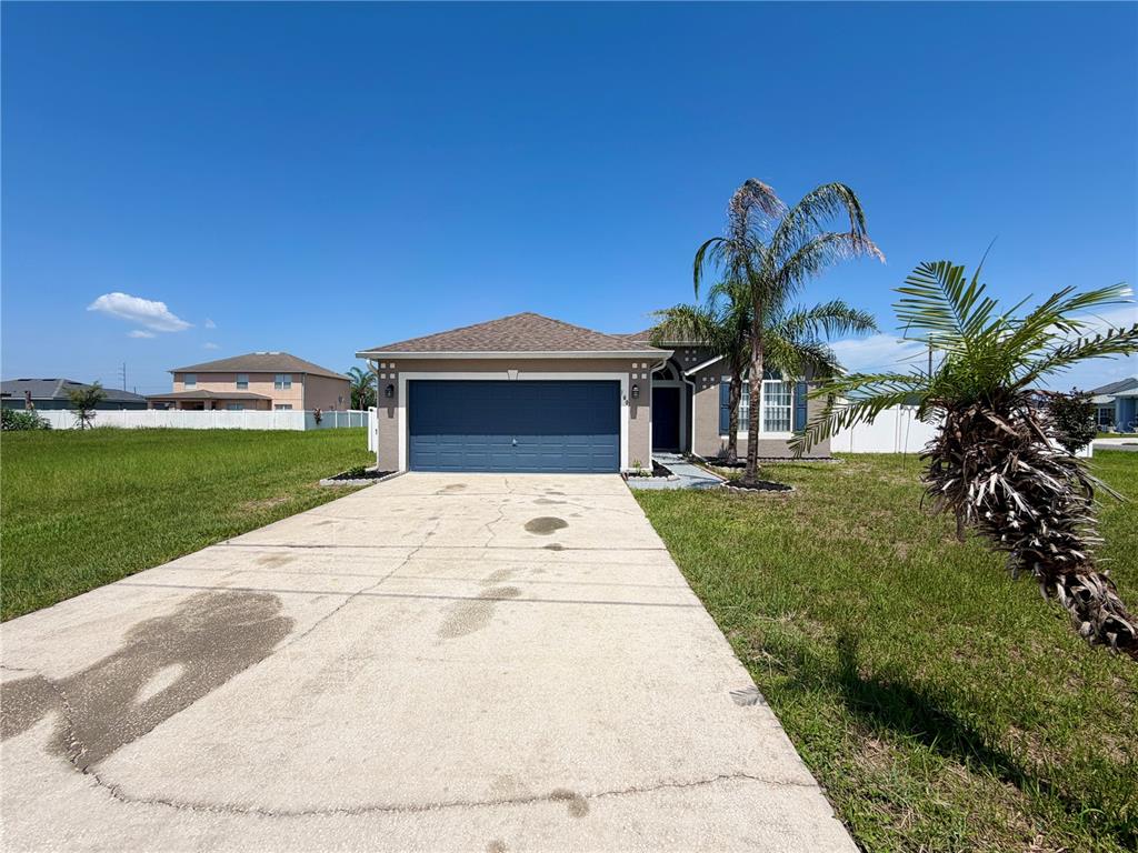 A single-story house with a blue garage door and a concrete driveway under a sky — 100 CIMARRON LANE, POINCIANA, FL