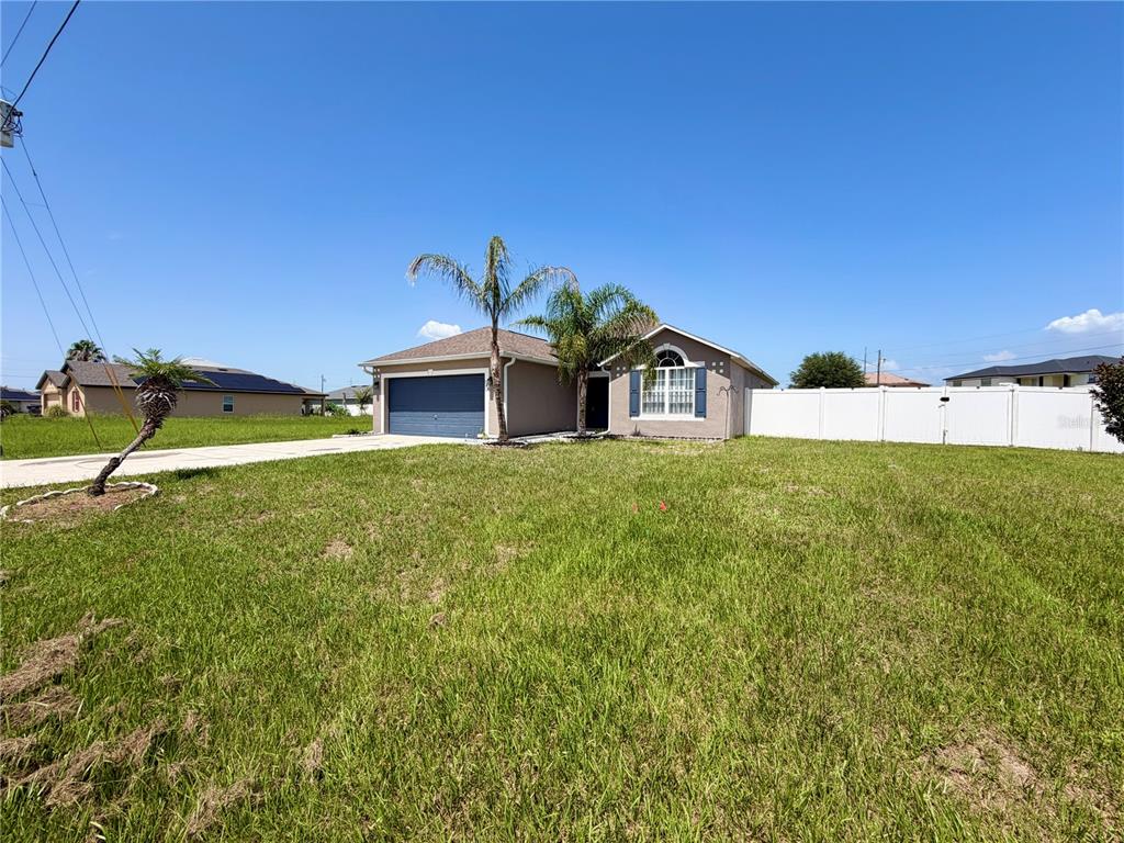 A single-story house with a blue garage door and a white fence under a clear sky — 100 CIMARRON LANE, POINCIANA, FL