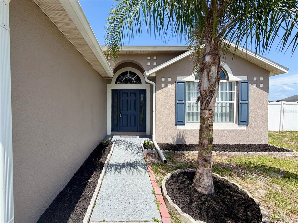 A tan house exterior features a blue front door, a palm tree, and a walkway — 100 CIMARRON LANE, POINCIANA, FL