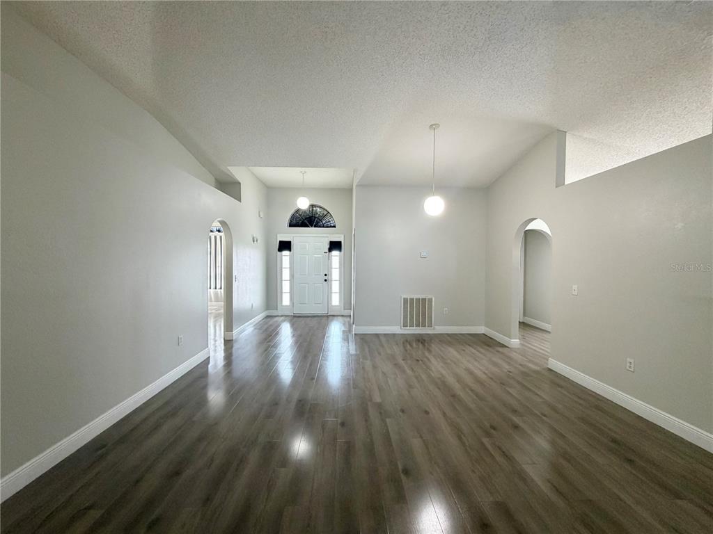 A bright, open-concept living area features light gray walls, wood-look flooring, and a front entryway — 100 CIMARRON LANE, POINCIANA, FL