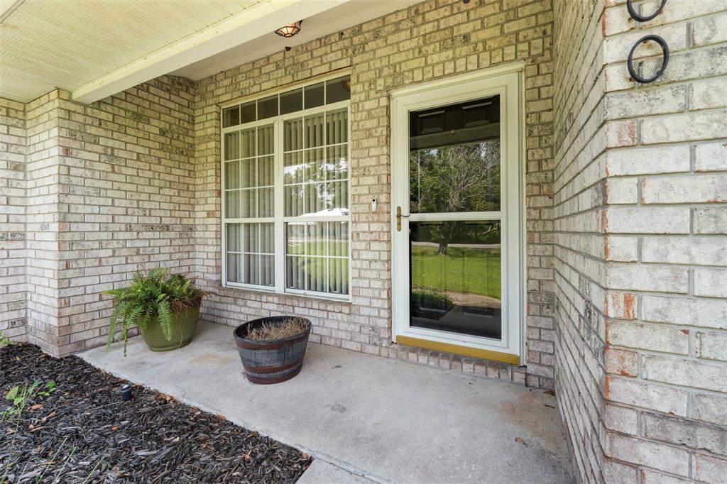 A brick house exterior features a concrete porch, a front door, and a large window — 200 NW CHARLOTTE GLEN, LAKE CITY, FL