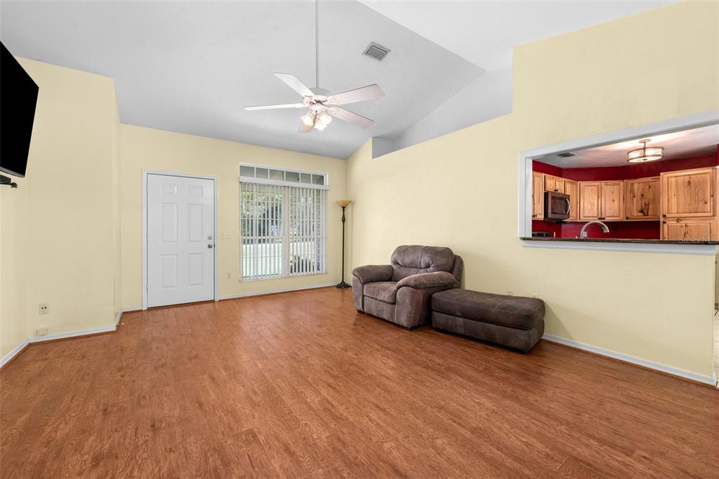 A living room with light yellow walls, wood-look flooring, a ceiling fan, and a pass-through window — 200 NW CHARLOTTE GLEN, LAKE CITY, FL