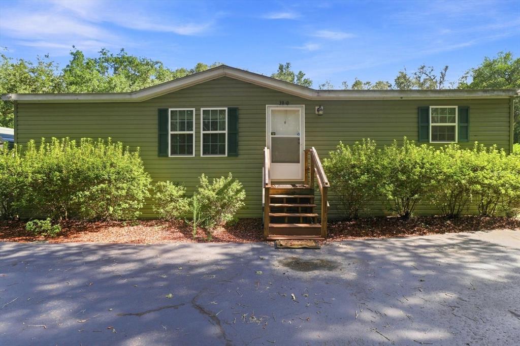 A green single-story manufactured home features a front entrance with wooden steps and bushes — 3970 SW 45TH AVENUE, BUSHNELL, FL