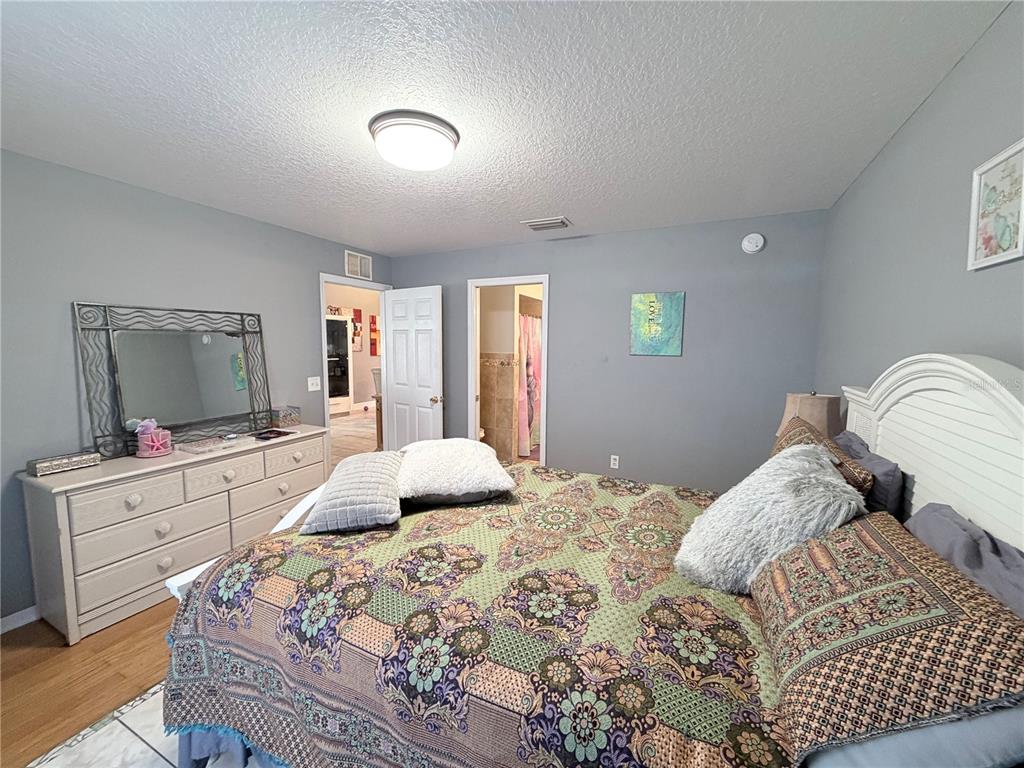 A bedroom features a bed with a patterned quilt, a dresser with a mirror, and doorways — 164 MARION OAKS LANE, OCALA, FL