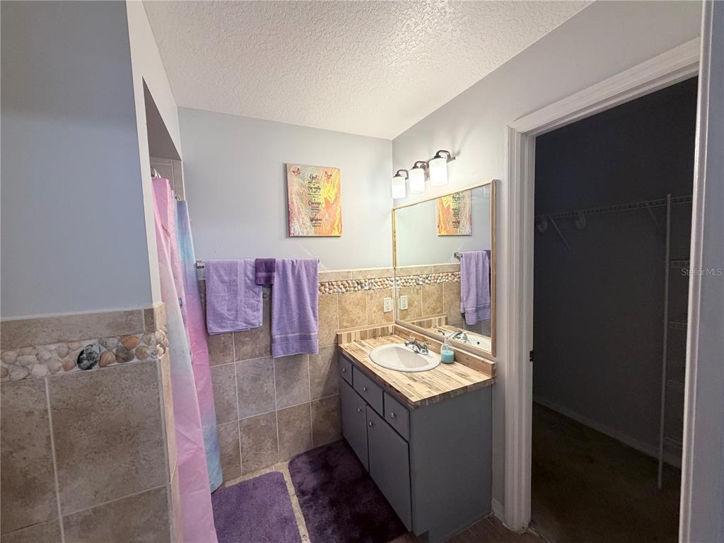 A bathroom features a gray vanity, a tiled backsplash, purple towels, and a walk-in closet — 164 MARION OAKS LANE, OCALA, FL