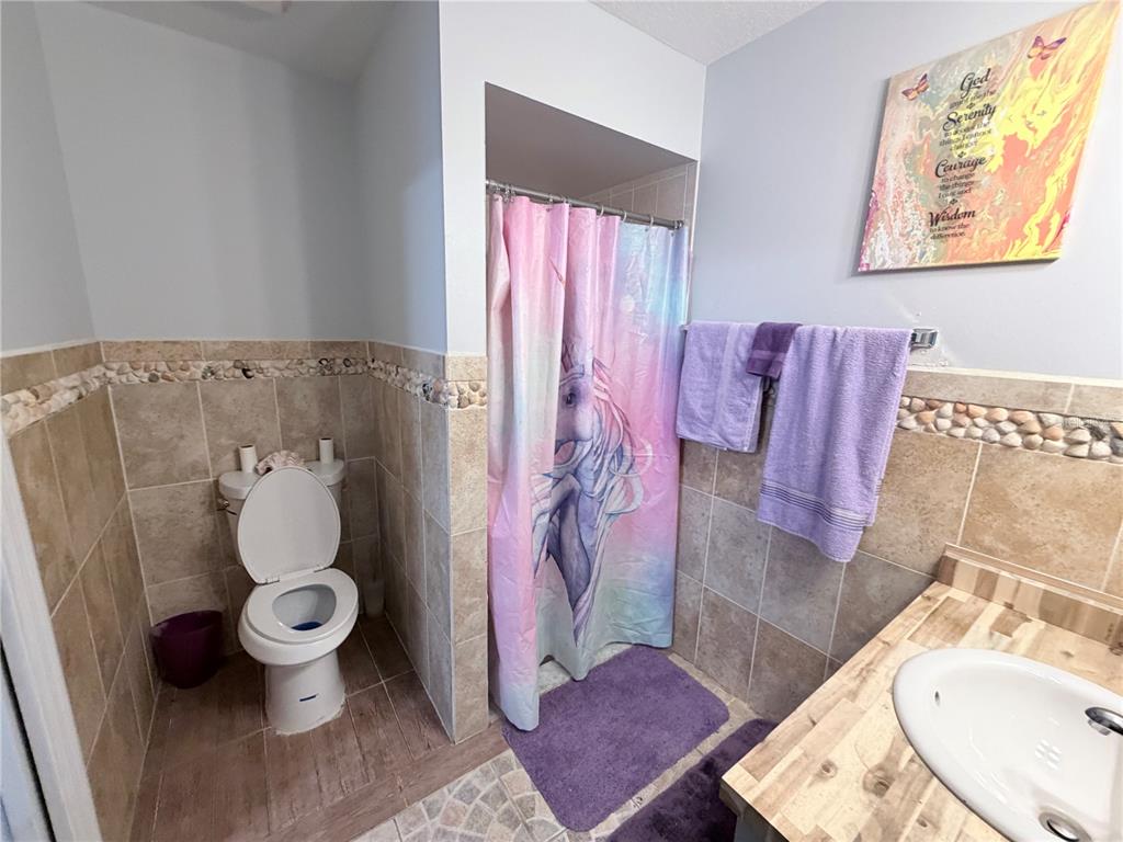 A bathroom features a unicorn shower curtain, beige tiled walls, and a wooden vanity top — 164 MARION OAKS LANE, OCALA, FL