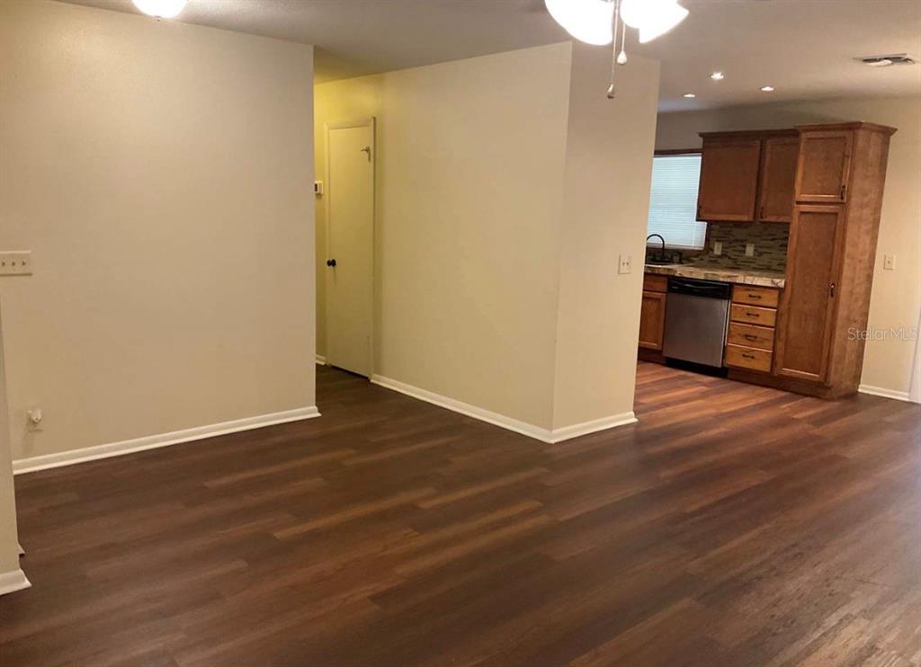 A kitchen with wood cabinets and a dishwasher opens into a living area with flooring — 2102 MONTANA STREET, ORLANDO, FL