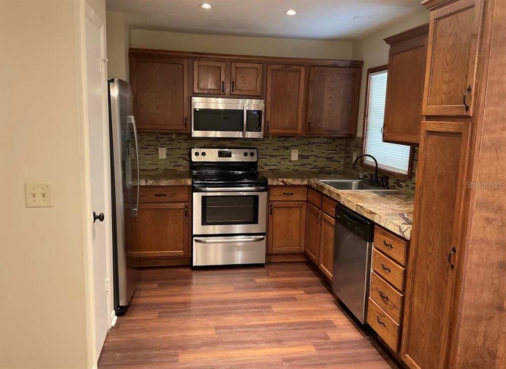 A kitchen features wood cabinets, stainless steel appliances, a tiled backsplash, and wood-look flooring — 2102 MONTANA STREET, ORLANDO, FL