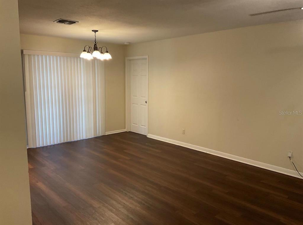 An empty room with dark wood-look flooring, beige walls, and a hanging light fixture — 2102 MONTANA STREET, ORLANDO, FL
