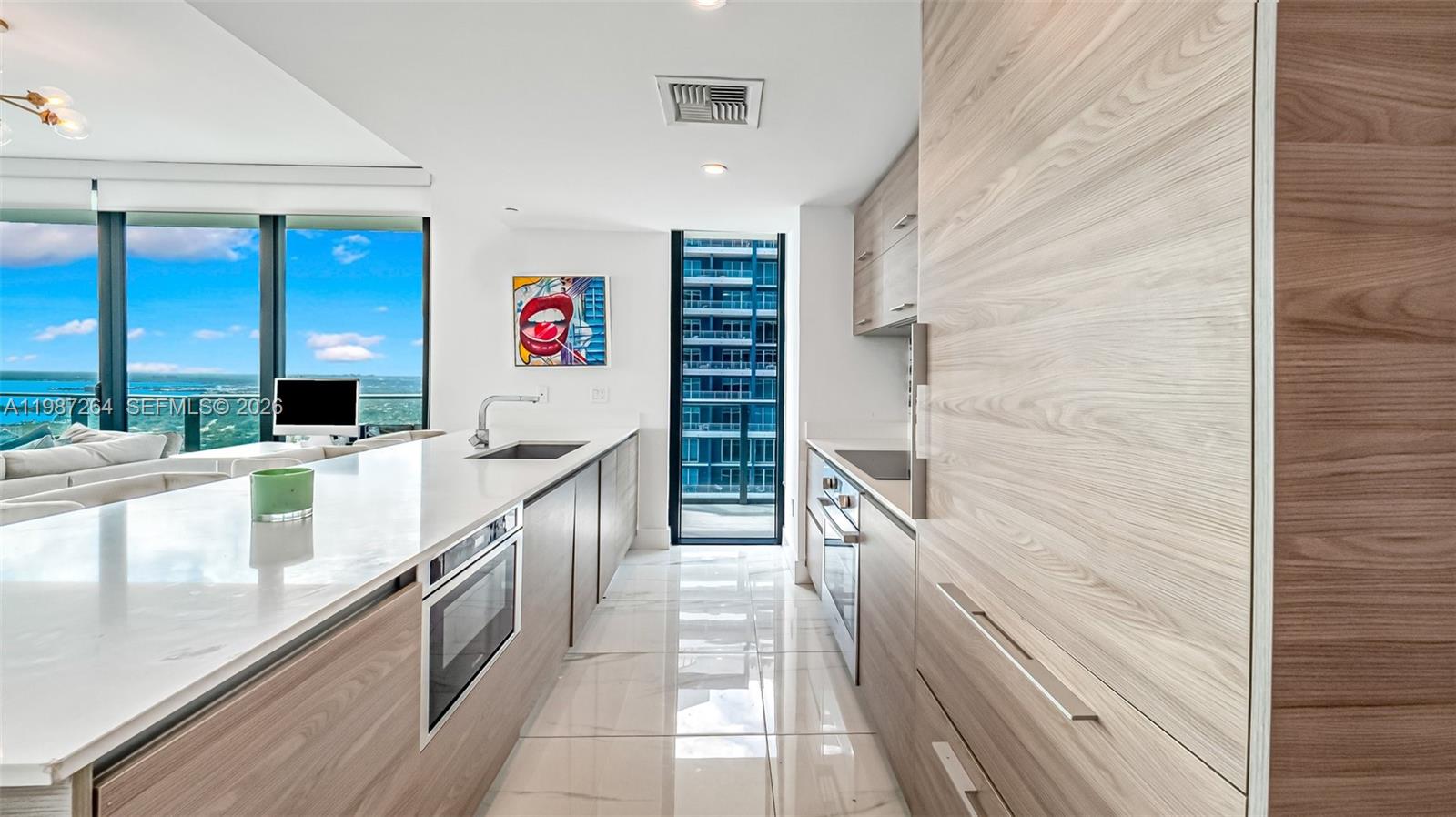 A modern kitchen features wood-grain cabinetry, white countertops, and a view of the ocean — 1300 S Miami Ave # 4306, Miami FL 33130, MIAMI, FL