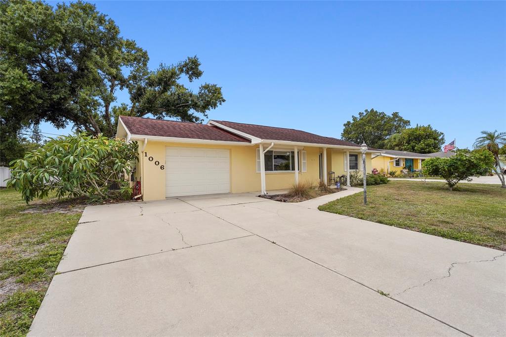 A yellow single-story house features a white garage door and a concrete driveway — 1006 DE LEO DRIVE, SARASOTA, FL