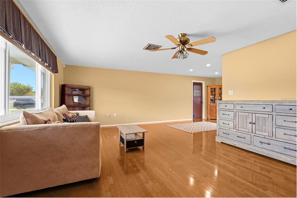 A living room with hardwood floors, a beige sofa, a coffee table, and a dresser — 1006 DE LEO DRIVE, SARASOTA, FL