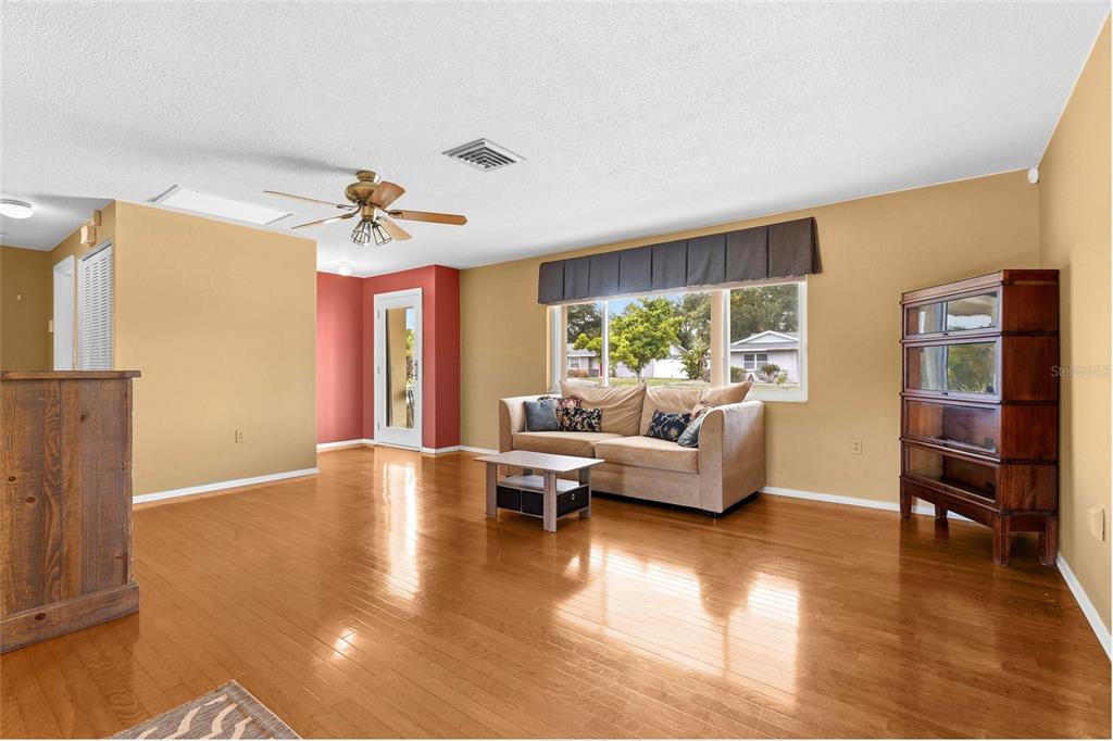 A living room with hardwood floors, a beige sofa, and a tall wooden cabinet — 1006 DE LEO DRIVE, SARASOTA, FL