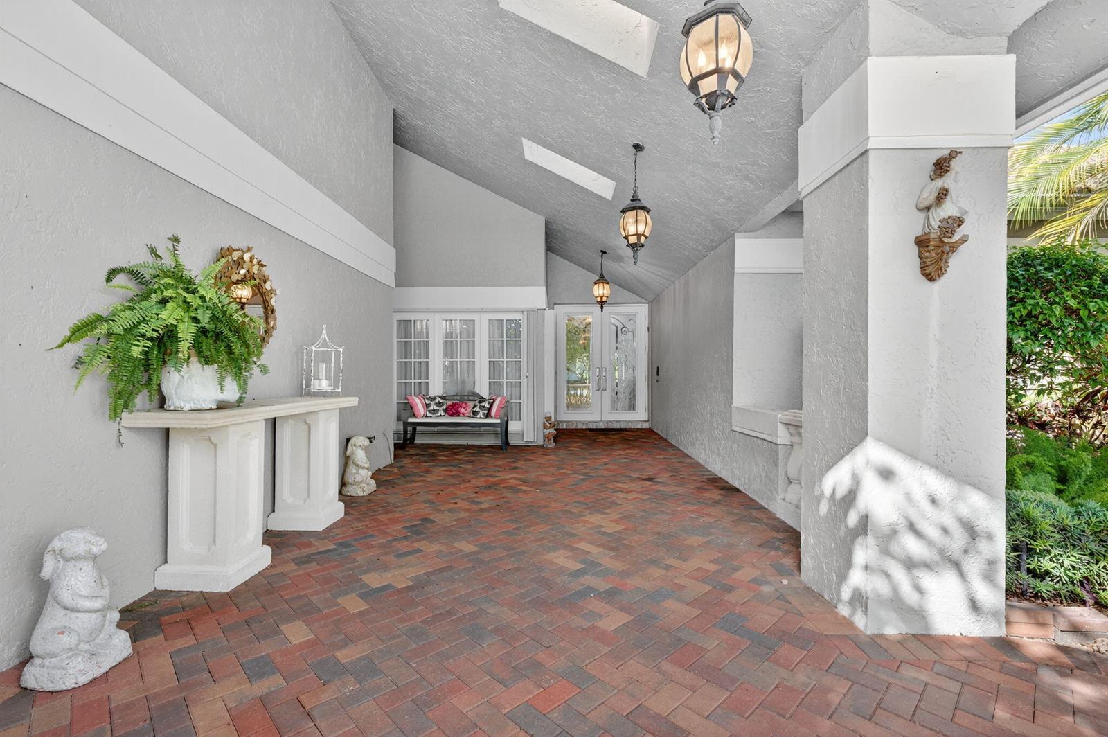 A covered brick patio leads to a glass-paned double door entrance with hanging lanterns — 7205 Mandarin Drive, Boca Raton FL 33433, BOCA RATON, FL