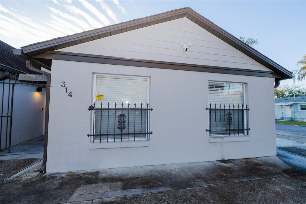 The exterior of a single-story house features light-colored stucco walls and two windows with grilles — 314 ALMA STREET, KISSIMMEE, FL