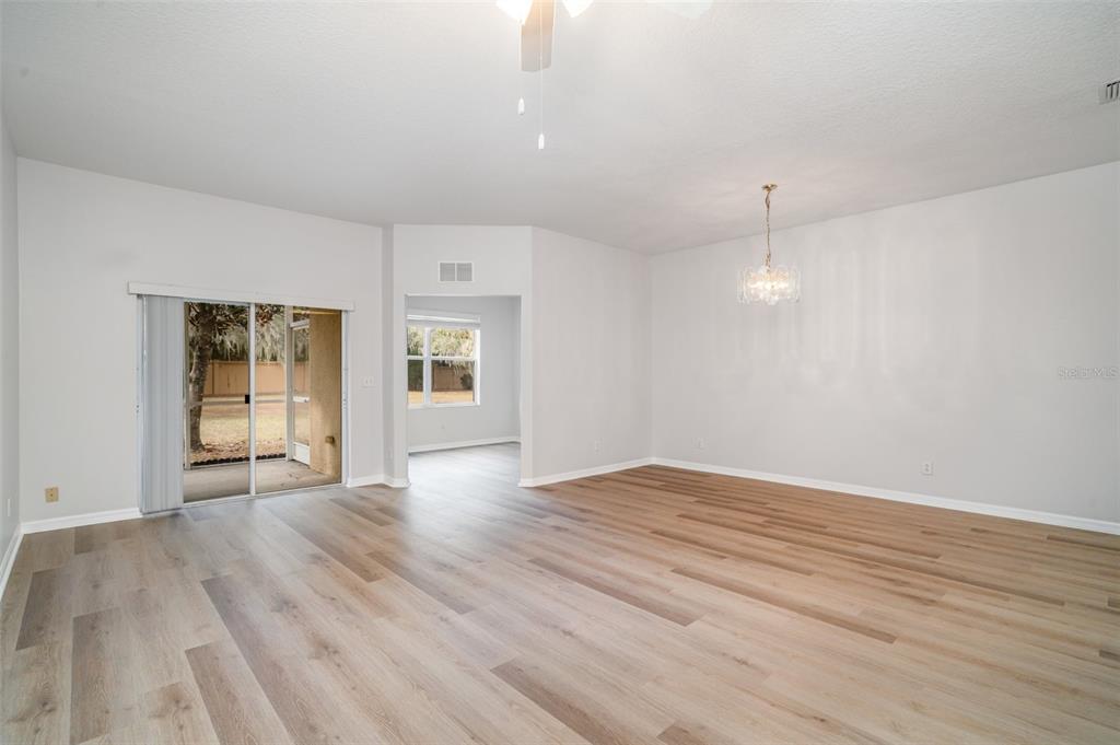 A spacious living area features light wood-look flooring, a ceiling fan, and a sliding glass door — 9317 STONE RIVER PLACE, RIVERVIEW, FL