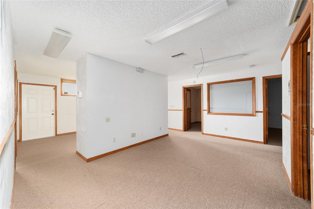 An interior room with beige carpet, white walls, wood trim, and fluorescent ceiling lights — 2801 SW COLLEGE ROAD UNIT 5, OCALA, FL