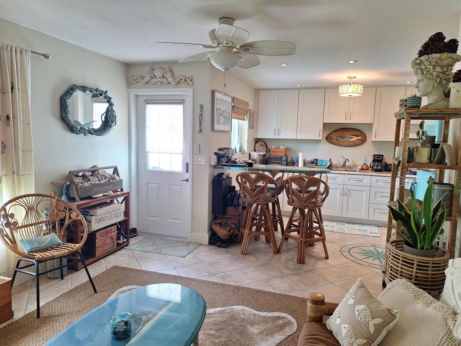 A coastal-style living room and kitchen area featuring rattan chairs, white cabinets, and tile flooring — 217 SE 2nd Avenue, Boynton Beach FL 33435, BOYNTON BEACH, FL