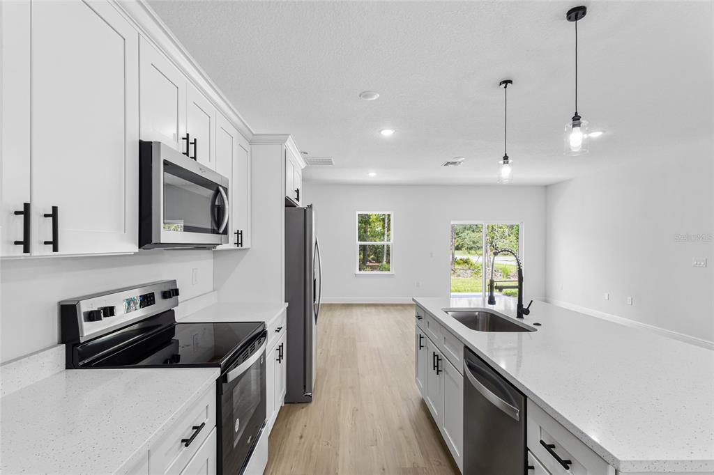 A modern kitchen features white cabinets, stainless steel appliances, a center island, and light flooring — 1071 W HAMPSHIRE BOULEVARD, DUNNELLON, FL